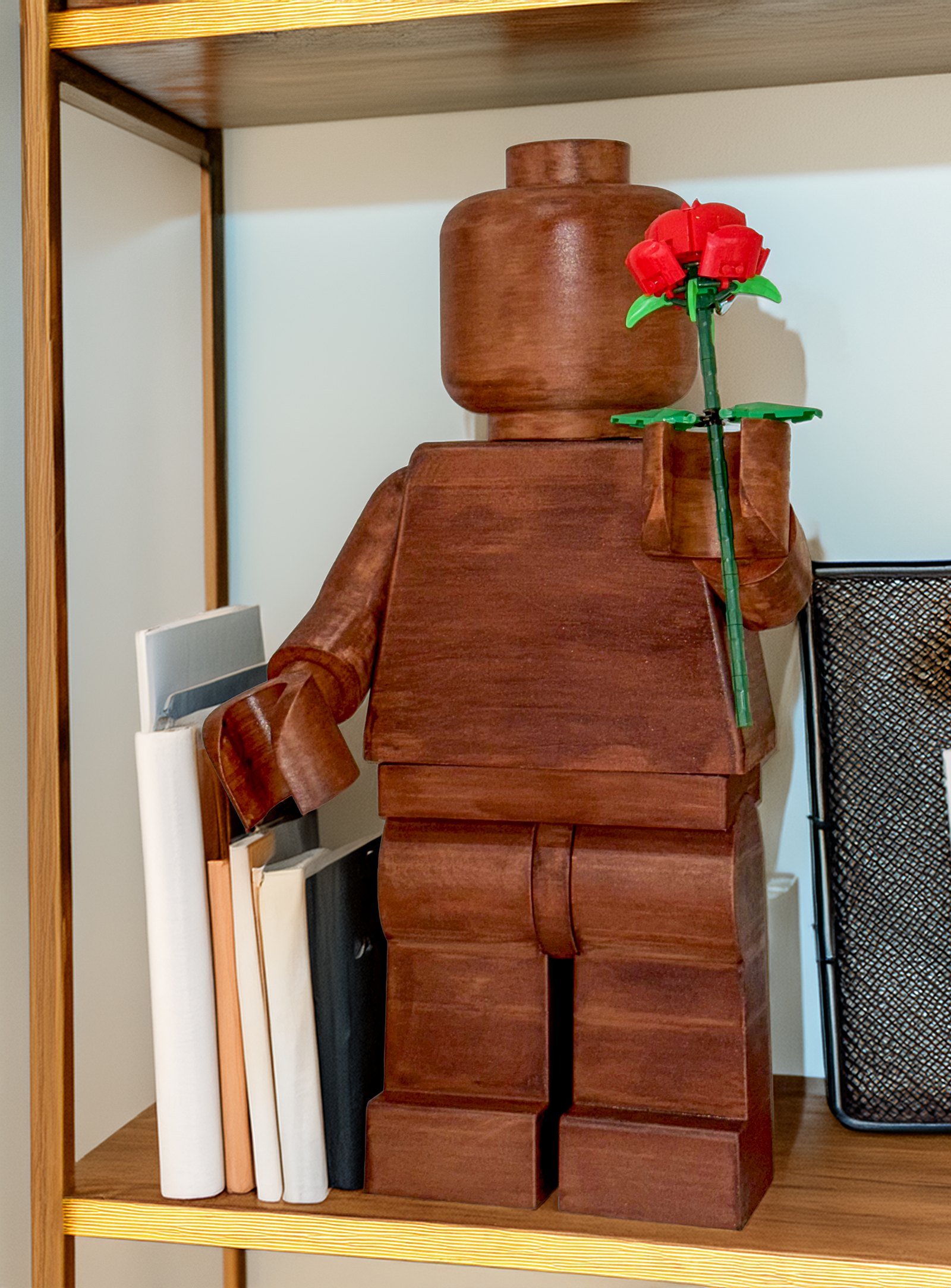 The Wood Edition on a lit bookshelf beside a row of books, holding a single red rose